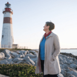 Leitstern. Leuchturm Eine Frau steht am Meer und blickt auf einen Leuchtturm.